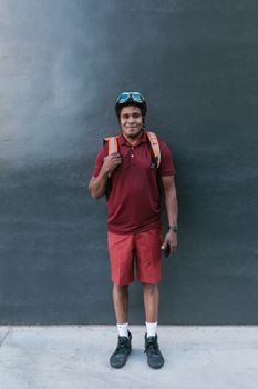 Smiling courier in maroon attire against dark wall, ready for delivery.