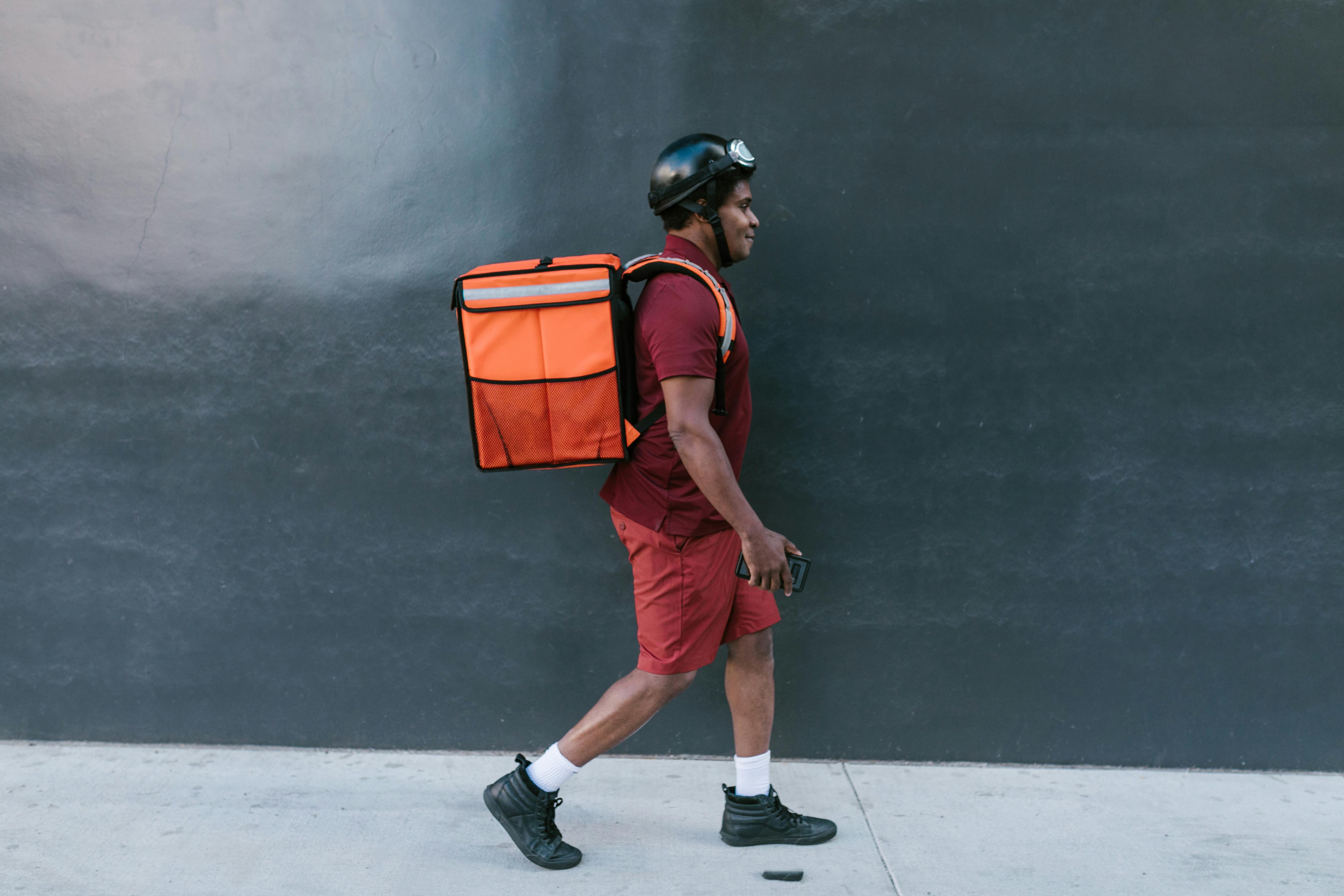 man in maroon polo shirt walking wearing food delivery bag