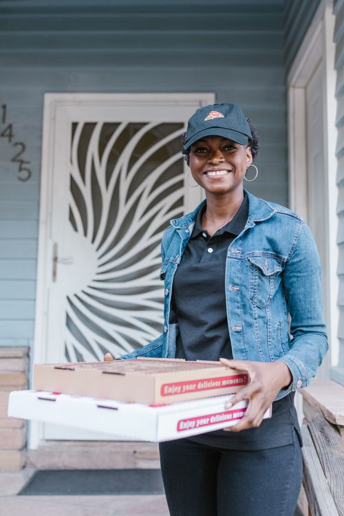 Free Smiling woman delivering pizza, wearing a cap and denim jacket, outdoors. Stock Photo