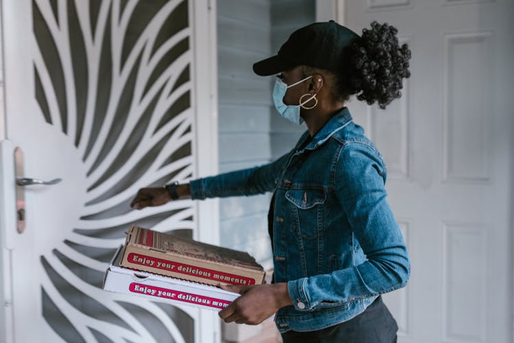 Woman In Blue Denim Jacket Standing Near The Door Carrying Pizza Boxes 