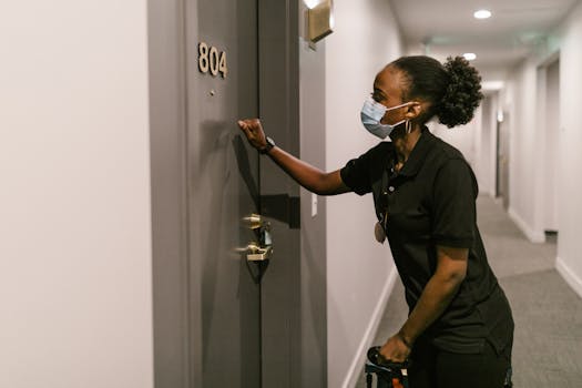 A delivery woman wearing a mask knocks on a door in an indoor hallway, promoting safety and logistics.