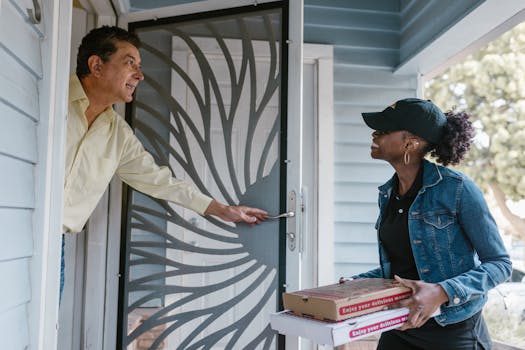 Delivery woman passing pizza boxes to smiling customer at front door.