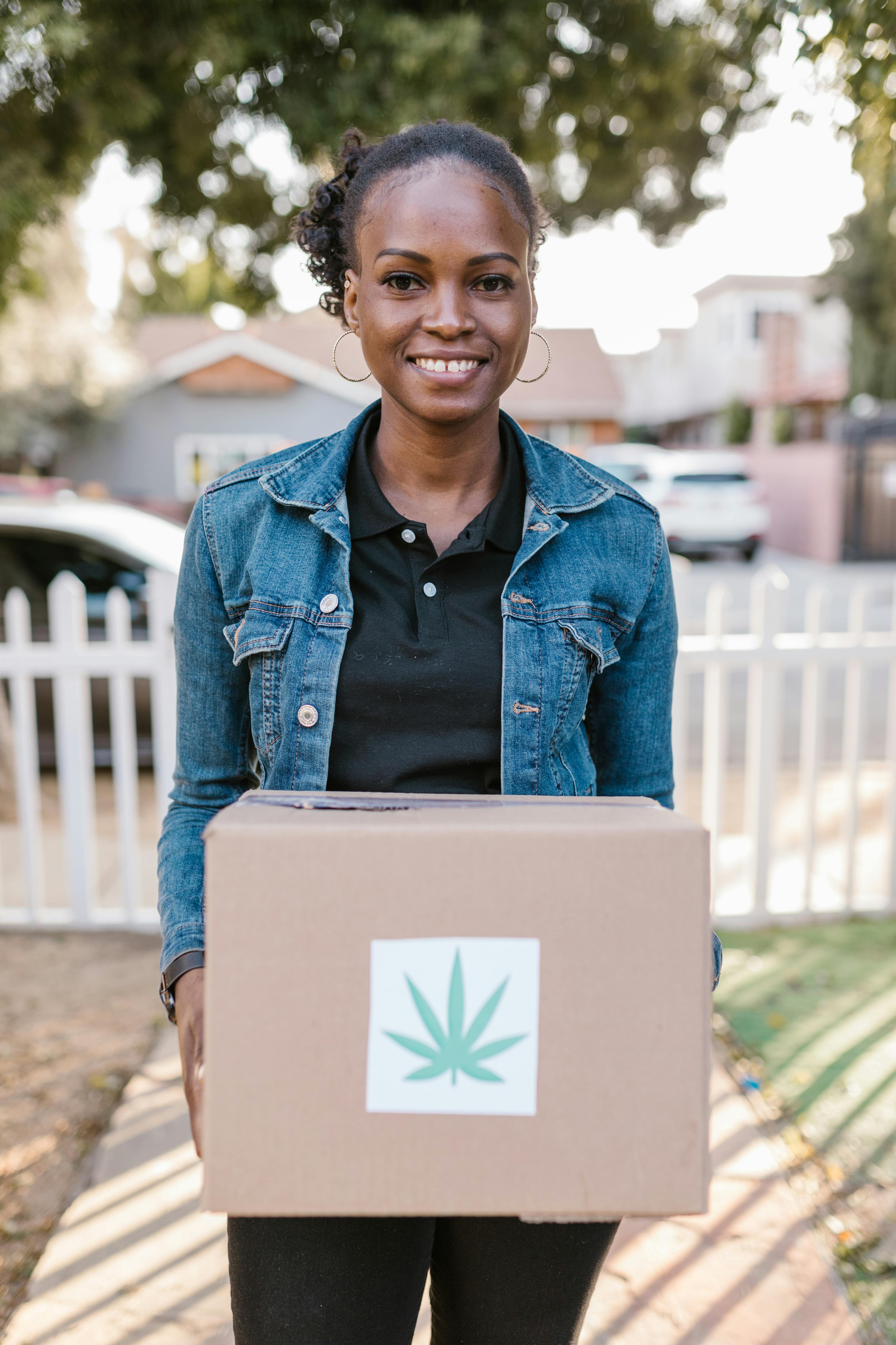 a woman carrying a box with a cannabis leaf sticker