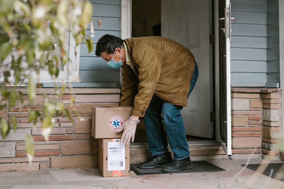 マスクを着用した男性がCOVID-19のための接触なしの安全のために玄関に荷物を配達しています。