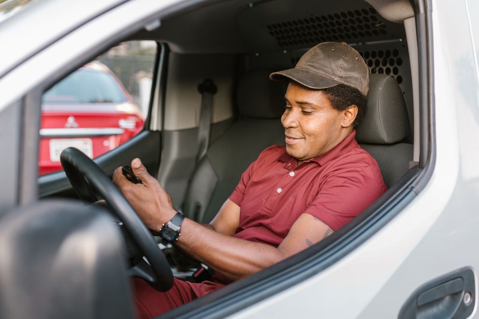 A man in a red shirt, sitting inside a van, using a smartphone, symbolizing modern delivery services. A man in a red shirt, sitting inside a van, using a smartphone, symbolizing modern delivery services.