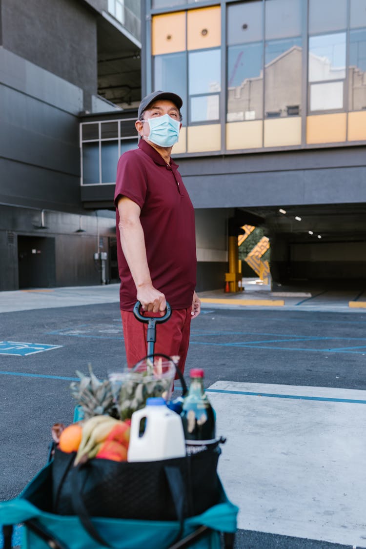 A Man In A Maroon Shirt Holding A Cart Of Groceries