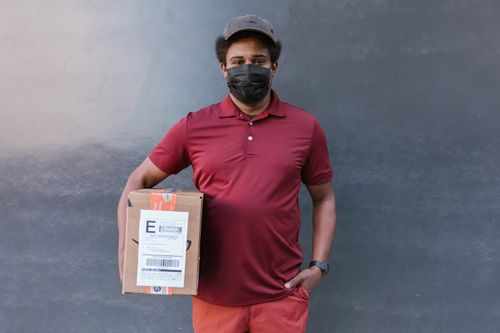 Free Courier in mask delivers package during pandemic, embracing new normal. Stock Photo