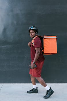 Side view of a delivery person with a backpack and helmet, ready for service.