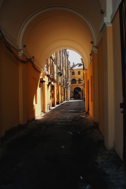 Free A sunlit passage through historical arches in an old city creates a picturesque urban scene. Stock Photo