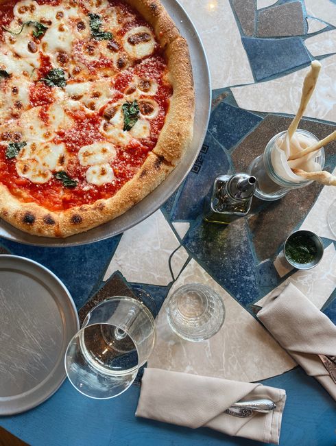 Top view of a margherita pizza with wine, set on a rustic table setting.