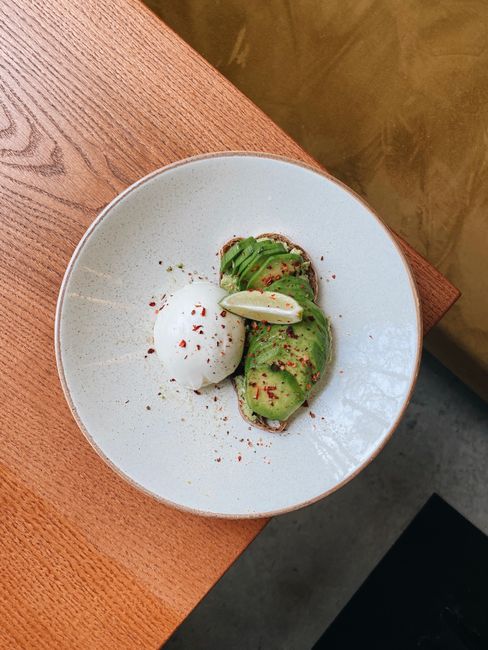 Stylish presentation of avocado toast with poached egg and lime on a wooden table.