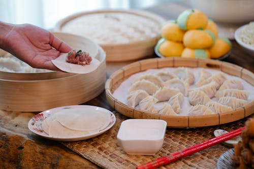 Free Crop unrecognizable cook filling and shaping dumpling and placing in bamboo steamer on table Stock Photo