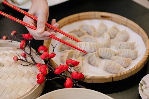 From above of crop unrecognizable worker taking dumpling from steamer with chopsticks near branch of Japanese cherry