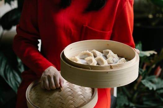 Woman in red holding bamboo steamer filled with dumplings.