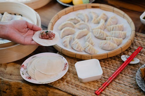 From above of crop anonymous female demonstrating dough circle with minced meat filling above table with dumplings at home