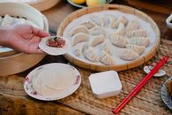 From above of crop anonymous female demonstrating dough circle with minced meat filling above table with dumplings at home