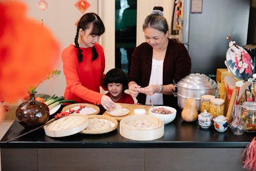 Content ethnic grandma with female teenager and grandson cooking dim sum at table with steamer in house