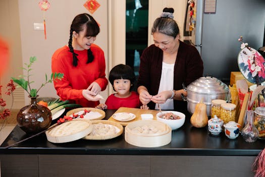 Cheerful Asian grandma with boy and female teen preparing dumplings at table with minced beef filling at home