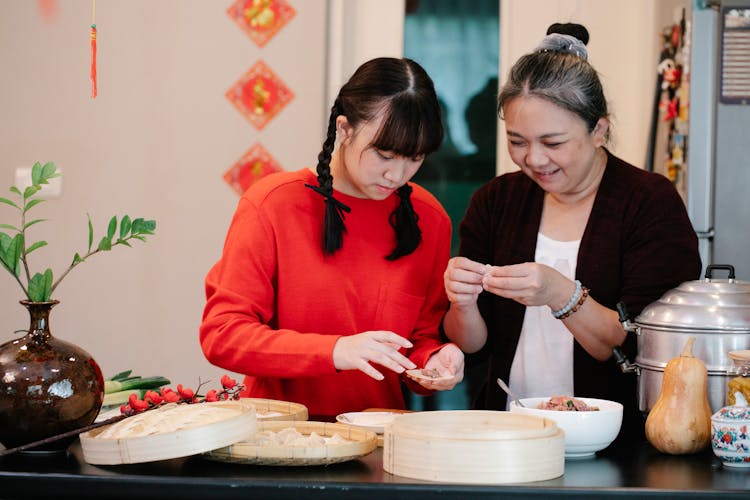 Smiling Ethnic Grandmother With Teenager Preparing Dumplings In House Kitchen