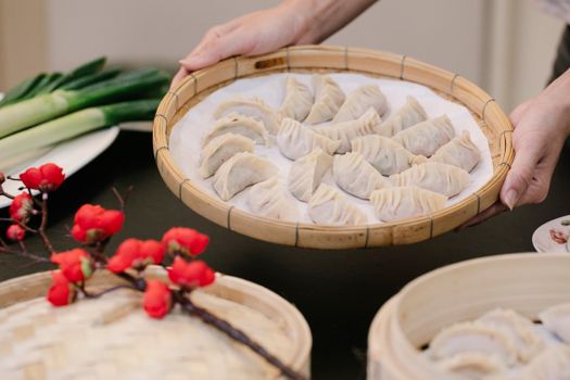 Crop unrecognizable female showing tasty dim sum on parchment paper in Asian tray in house