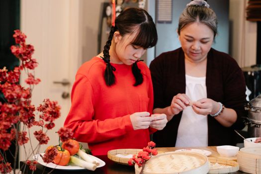 Ethnic grandma with teen preparing traditional oriental dish at table with fresh vegetables and steamer in house