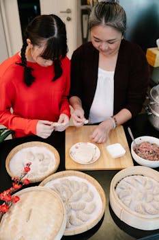 From above of Asian grandma with granddaughter cooking dumplings with ground meat filling at table in kitchen