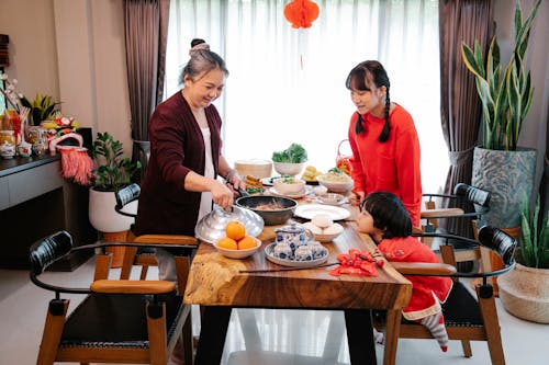 Smiling Asian grandmother with teen and boy serving delicious food
