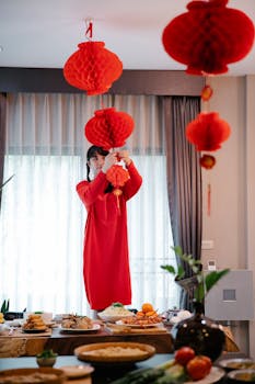 Woman in red dress hanging lanterns, preparing for a festive Lunar New Year meal indoors.
