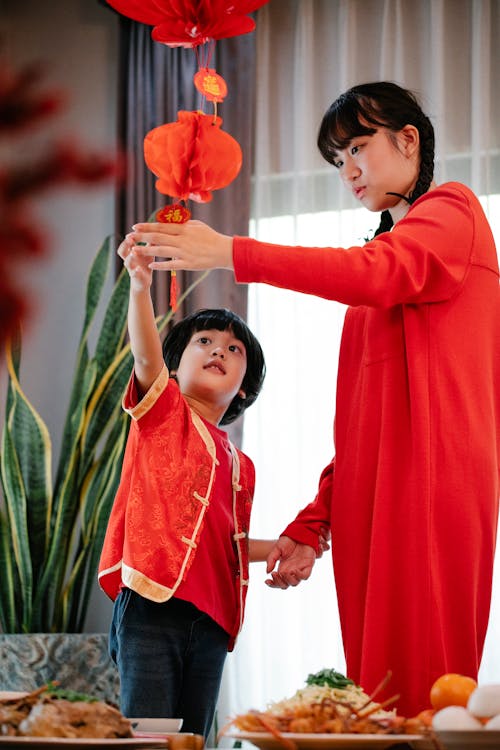 Asian teenager with brother decorating home with red lamps