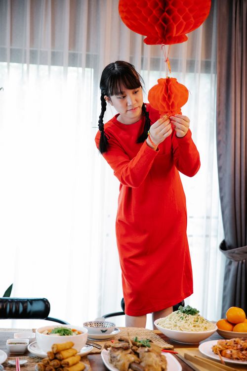 Free A young woman decorates for Lunar New Year with red lanterns, preparing a festive feast. Stock Photo