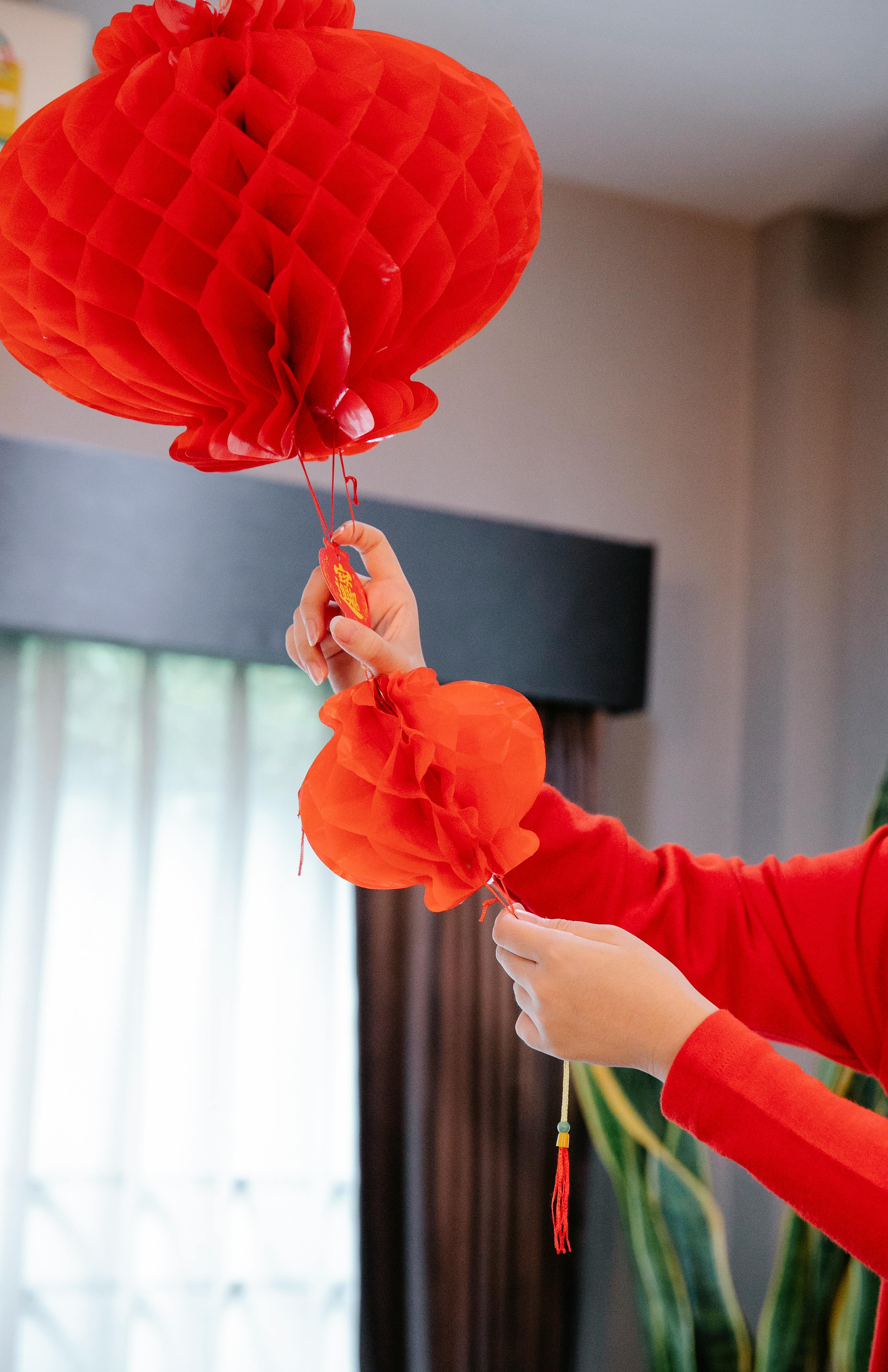 Person in red clothes hanging a vibrant red lantern indoors for Chinese New Year.