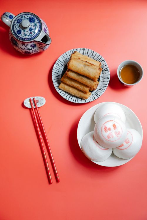 Free Top view of tasty Asian appetizers and steamed rice buns with hieroglyphs against ornamental teapot and chopsticks on red background Stock Photo