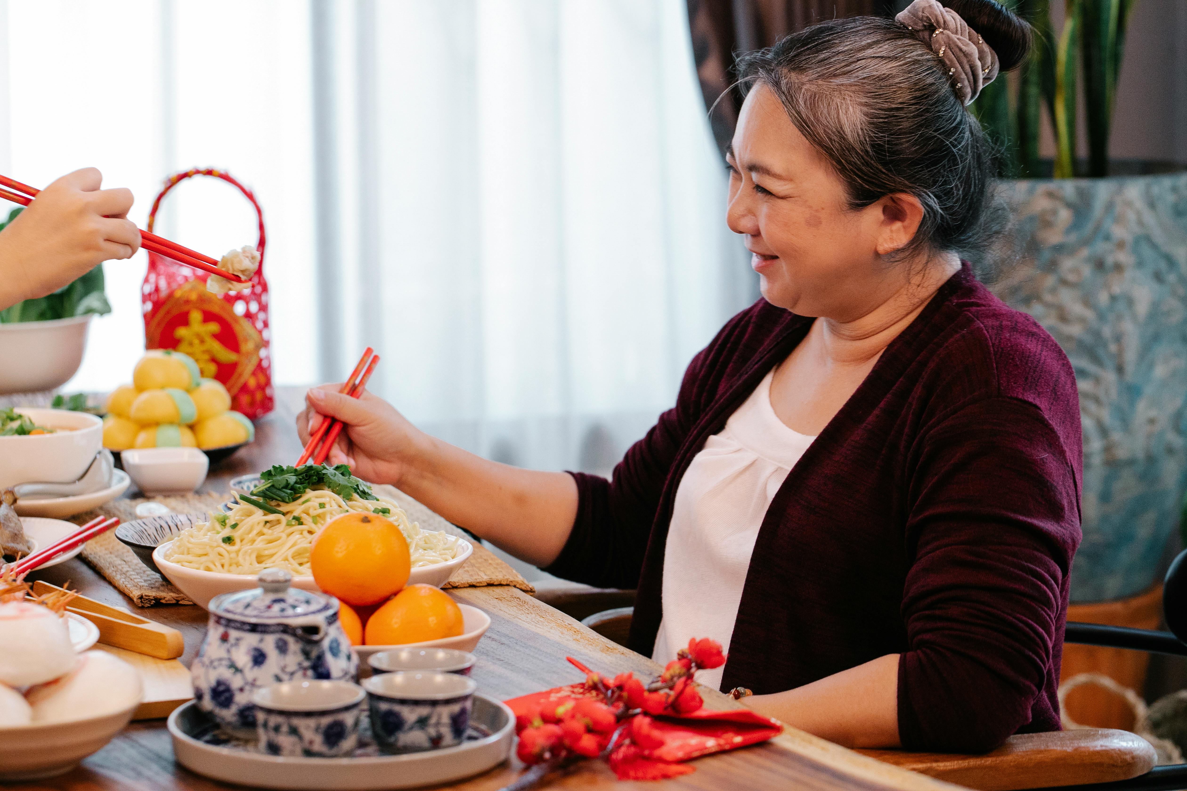 smiling asian woman interacting with crop relative at table