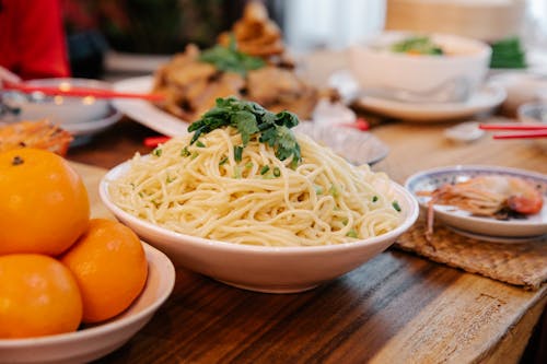 Free Tasty cooked noodles with fresh parsley leaves between prawn and ripe oranges on table in house Stock Photo