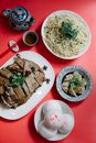 Top view of tasty oriental dishes of dumplings between steamed rice buns and noodles near tea on red background