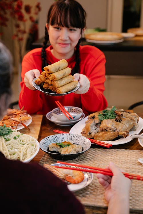 Smiling Asian teen with spring rolls talking to crop relative