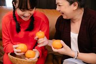 Crop happy Asian grandmother and granddaughter with oranges on sofa