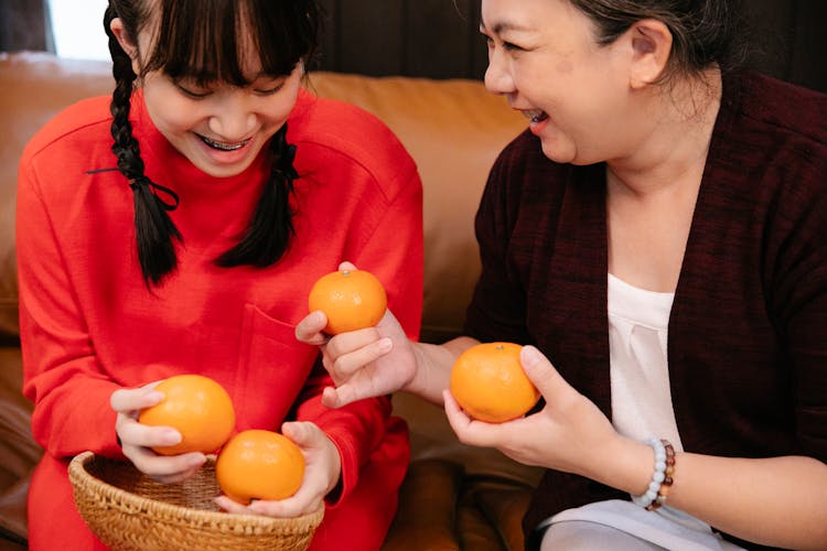 Crop Happy Asian Grandmother And Granddaughter With Oranges On Sofa