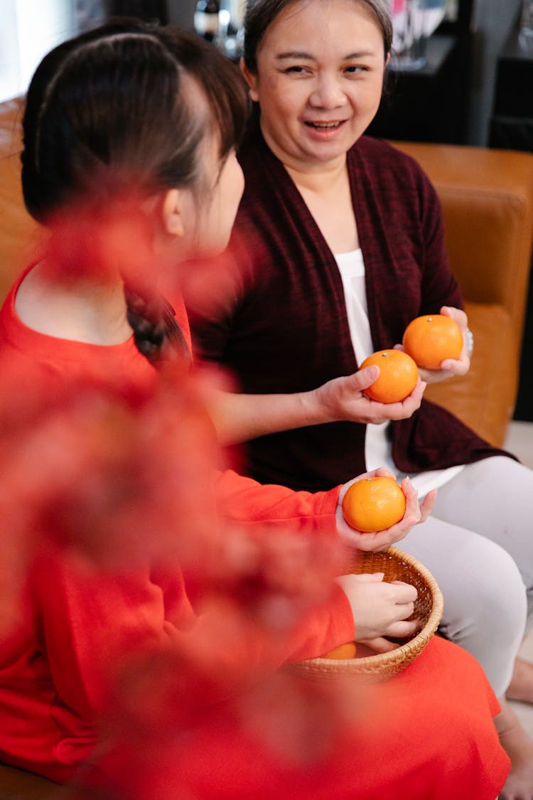 Crop Asian Grandmother With Oranges Talking To Granddaughter At Home