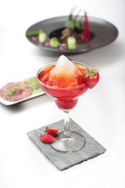 A tall glass filled with a swirled, two-toned frozen cocktail, creamy white piña colada on one side and bright pink strawberry daiquiri on the other, garnished with a pineapple wedge and cherry.