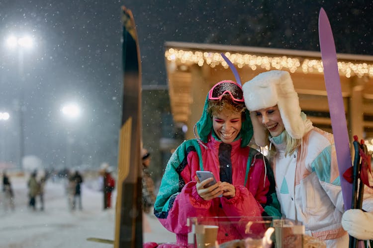 Two Women In Winter Clothes Looking At A Smartphone