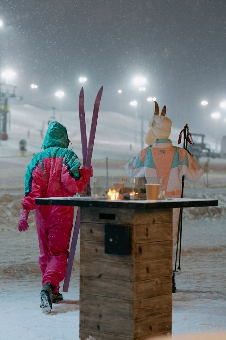 Two People In Ski Suits Holding Skis