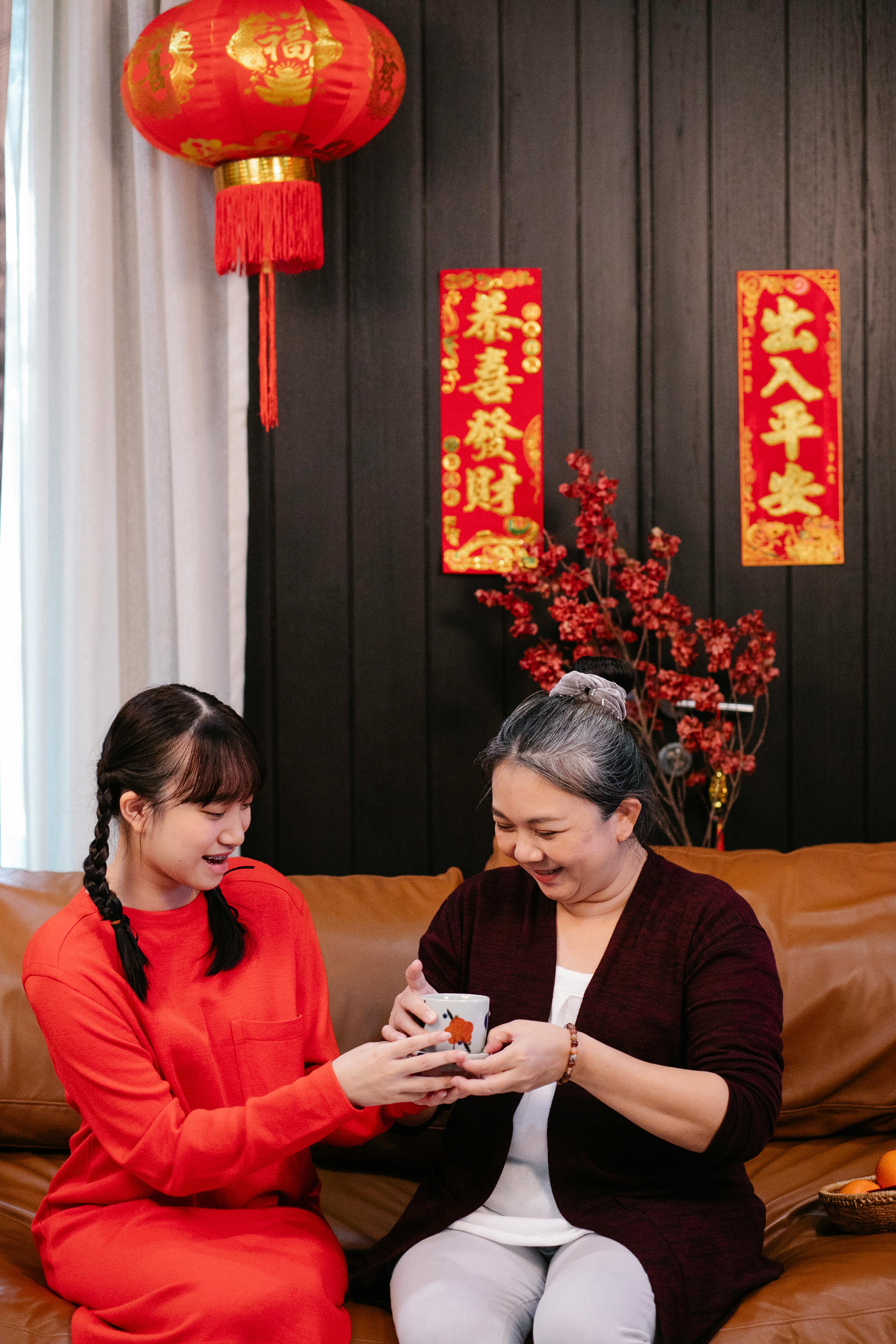 smiling asian teen passing gift cup to grandmother on sofa