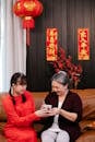 Smiling Asian teen passing gift cup to grandmother on sofa