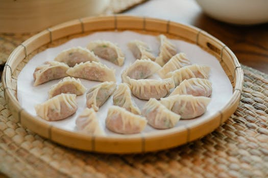 Uncooked Asian dumplings arranged on a bamboo tray with a parchment lining.