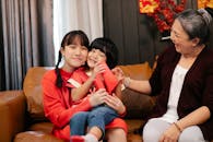 Cheerful Asian teen embracing brother against grandmother on sofa