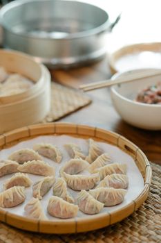 Dim sum with filling on parchment paper in tray on straw mat at home on blurred background