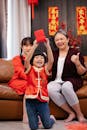 Excited ethnic child with red packet against female teenager and grandmother celebrating New Year holiday in house room