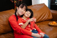 Smiling Asian teenager embracing brother on sofa during festive event
