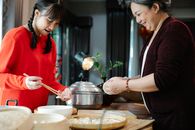Crop smiling ethnic grandmother with granddaughter cooking Chinese dumplings at table with bamboo tray in house